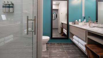A modern bathroom with a glass shower enclosure, a toilet, a sink with a mirror, and a wooden bench.