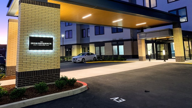 Entrada de un hotel con un corredor cubierto, un automóvil estacionado al frente y un letrero que dice "The Independence A Trace Hotel".