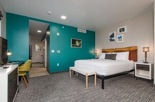 Una habitación de hotel con cama, mesitas de noche, un escritorio con silla y un pequeño banco.