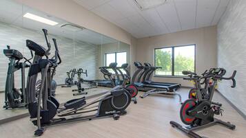 A gym with various exercise machines, large windows, and a mirrored wall.