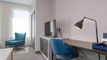A hotel room with a desk, two chairs, a TV, and a lamp.