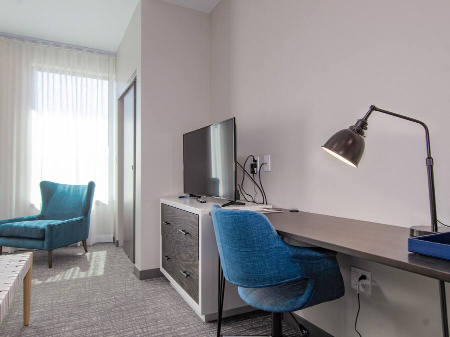 A hotel room with a desk, two chairs, a TV, and a lamp.