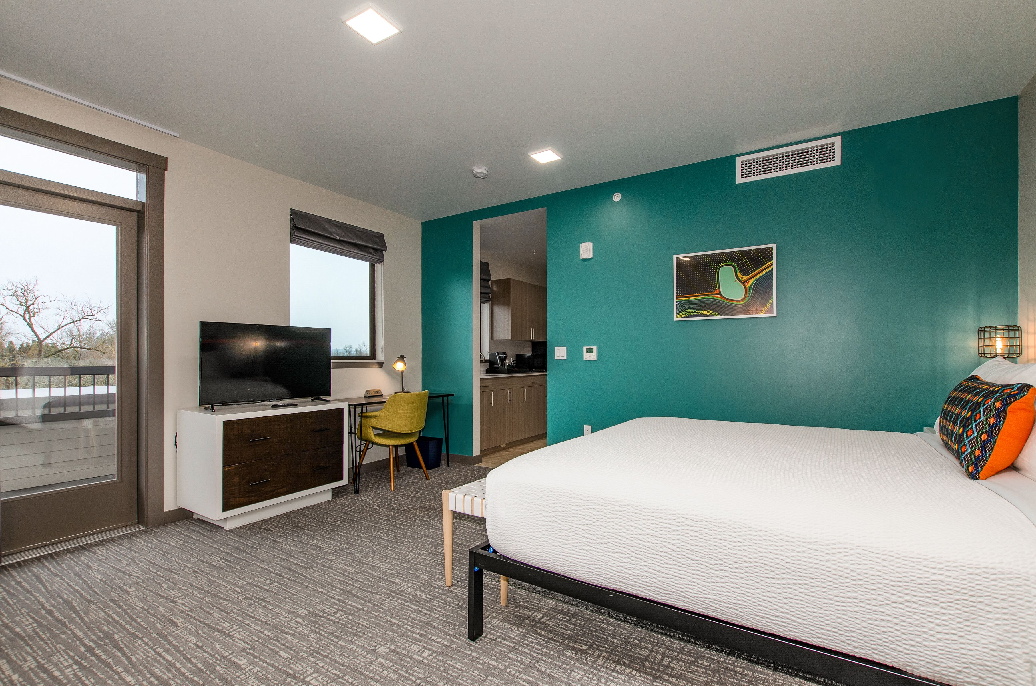 Een moderne hotelkamer met een bed, televisie, bureau en kitchenette.