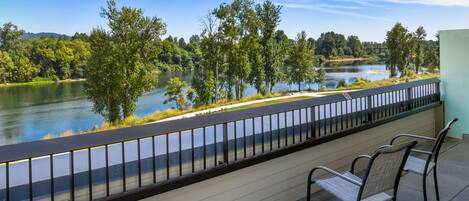 A balcony with a view of a lake, surrounded by trees, and featuring two chairs.