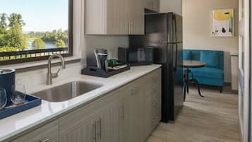 Una cocina moderna con un lavamanos, cafetera, microondas y refrigerador. Se ve una ventana con vista a árboles y un lago.