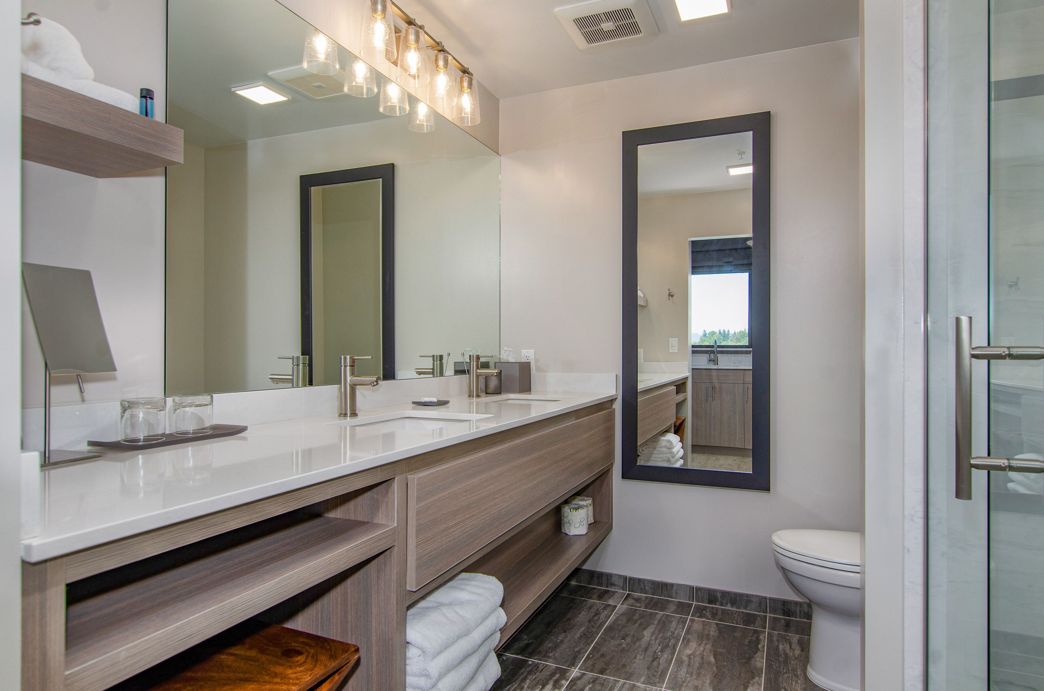 Un baño moderno con lavamanos dobles, un espejo grande, inodoro y cabina de ducha de vidrio.