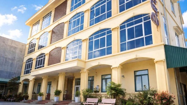 Un hotel de varios pisos con fachada amarilla, ventanas amplias y un área de entrada cubierta con bancos.