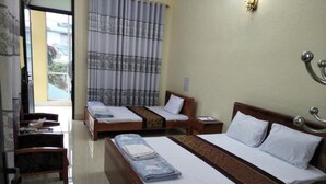 Habitación de hotel con dos camas individuales, una mesita de noche de madera, una silla y vistas al exterior a través de una ventana con cortinas.