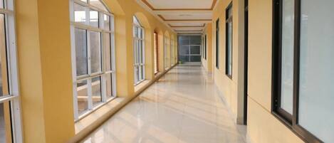 A long, narrow hallway with large windows on one side and a plain wall on the other.