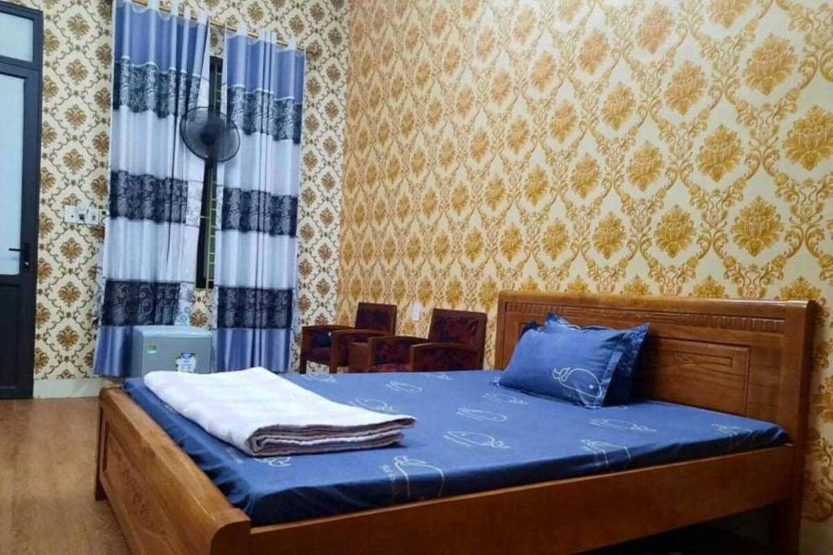 Une chambre avec un lit en bois, une petite table de chevet, une chaise et un rideau.