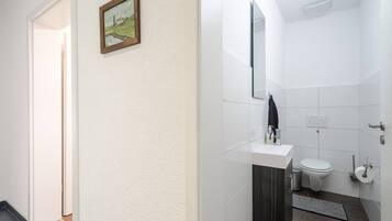 A bathroom with a white sink, toilet, and a mirror. There is a small rug on the floor and a picture frame on the wall.
