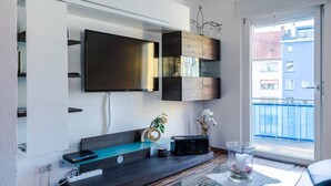 Ein modernes Wohnzimmer mit Flachbildfernseher, Holzausbau, einer Radioanlage und Blick auf Gebäude durch ein großes Fenster.