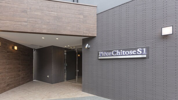 Una entrada moderna de edificio con un letrero que dice "Piece Chitose S1".