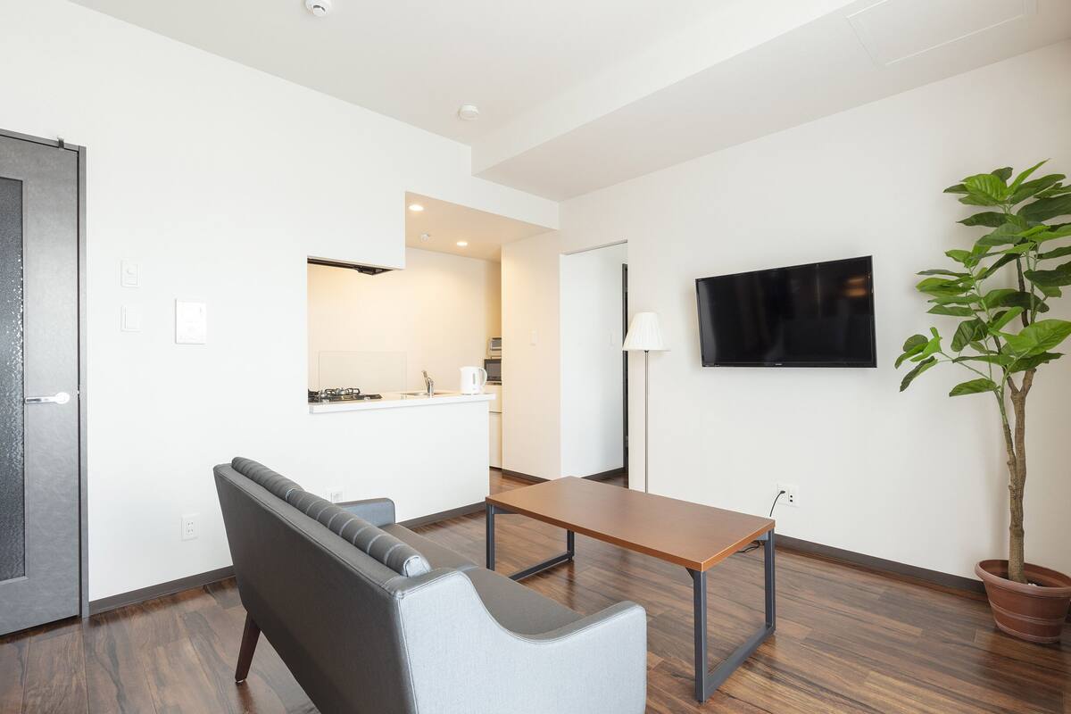 A modern living room with a sofa, a table, a potted plant, and a flat-screen TV mounted on the wall.