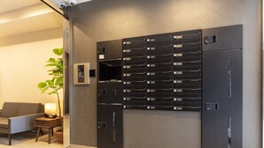Una zona de recepción moderna con un sistema de buzones empotrado en la pared, un sofá, una mesita con lámpara y una planta en maceta.