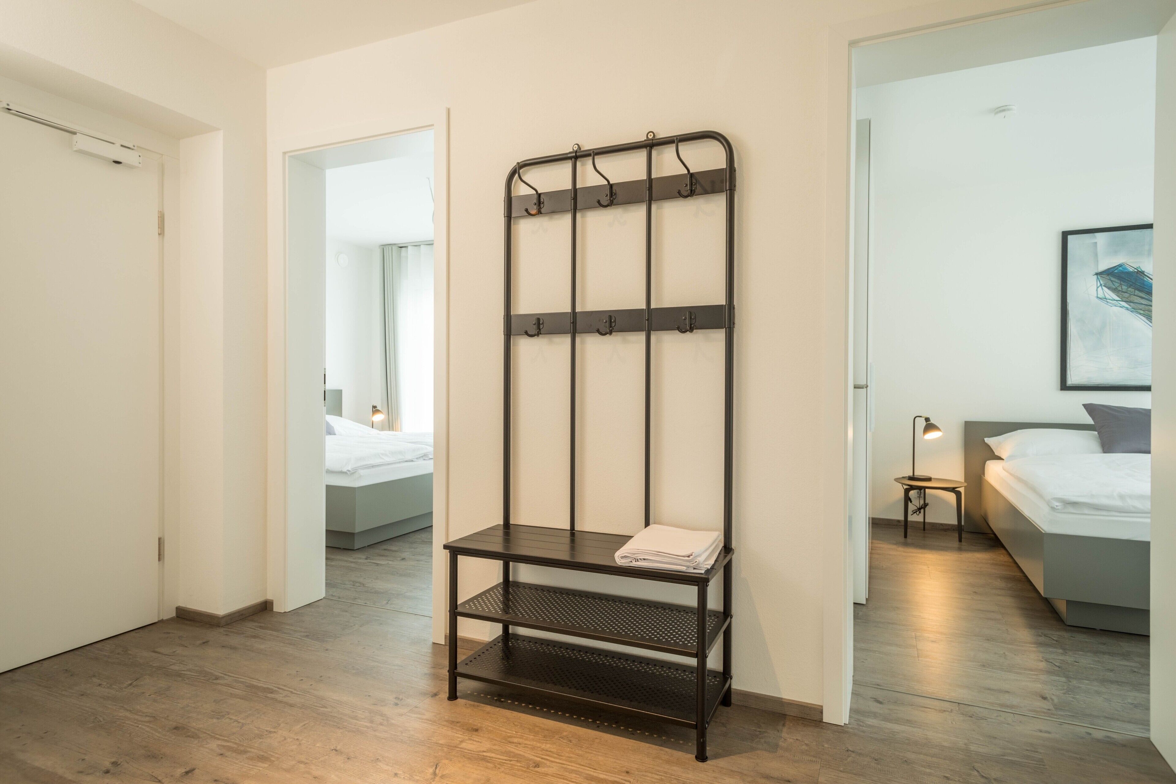 A hotel room with a metal rack, a bed, a nightstand, and a door.