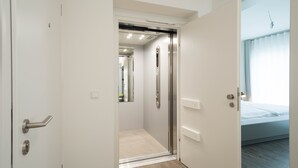 Ein modernes Hotelzimmer mit Dusche, Bett und Blick zum Himmel.