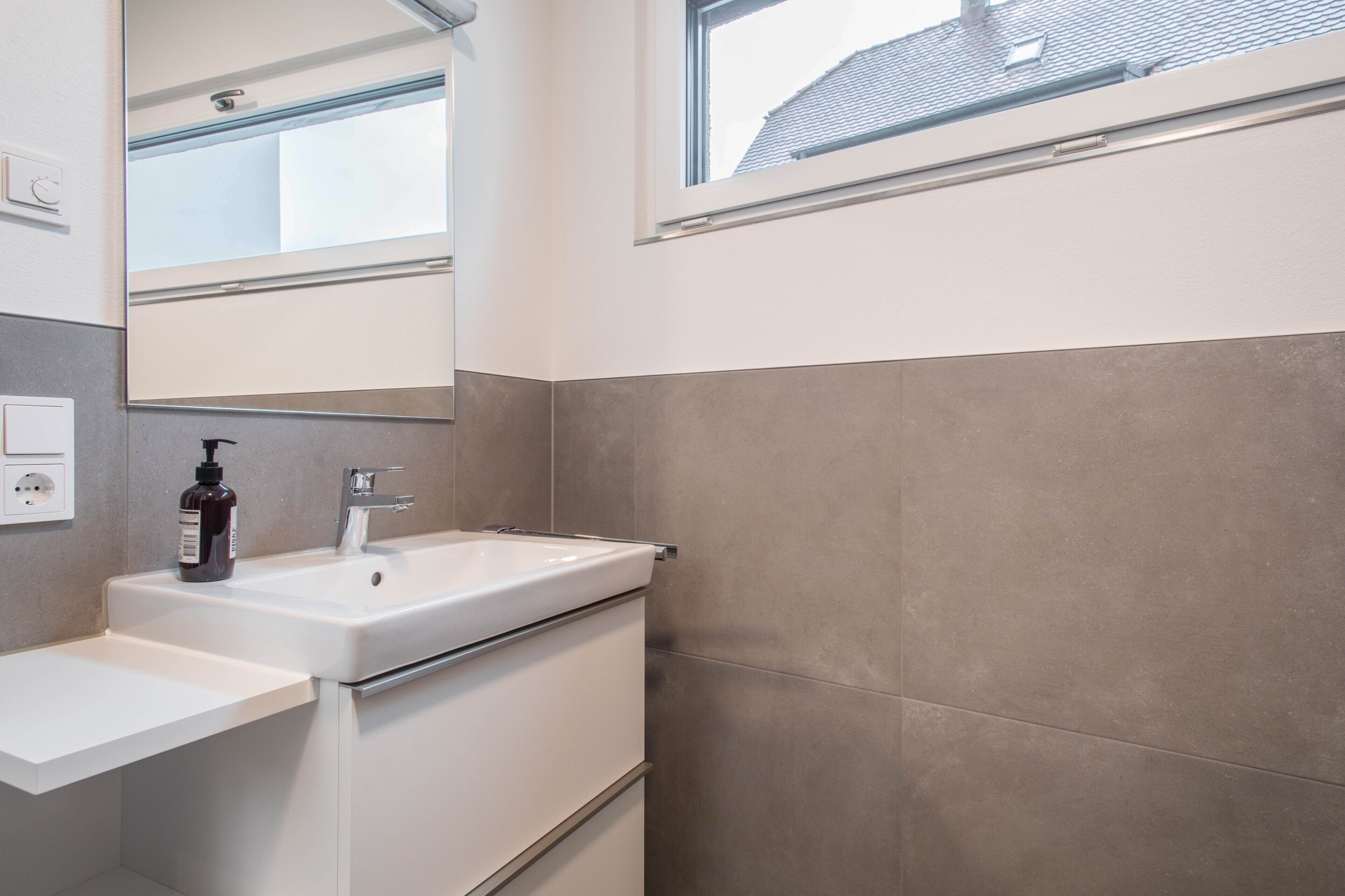 Ein modernes Badezimmer mit Waschbecken, Spiegel und Fenster.