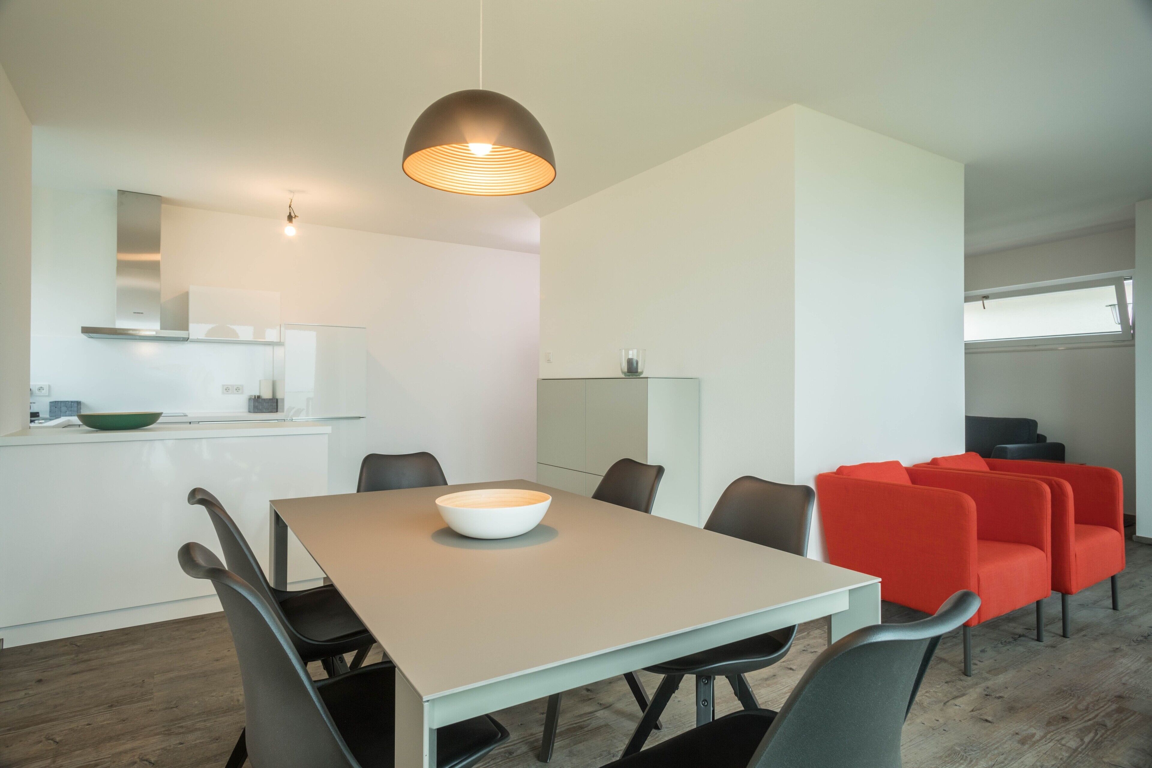 Uma sala de jantar moderna com uma mesa, cadeiras, uma tigela e uma luminária pendente.