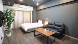 A modern hotel room with a bed, a leather sofa, a wooden coffee table, and a potted plant. - Piece Eniwa (Eniwa)