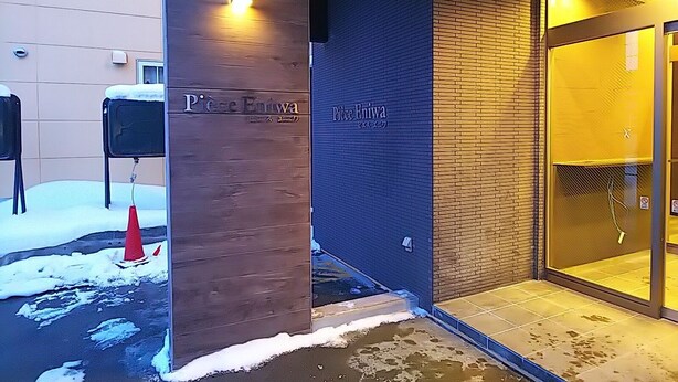 The entrance of a hotel with a sign reading "Piece Entrywa" and a brick wall. - Piece Eniwa (Eniwa)