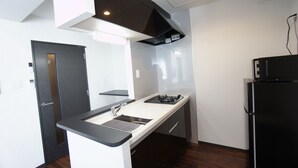 A compact kitchen with a built-in gas stove, a sink, and a black refrigerator. - Piece Eniwa (Eniwa)