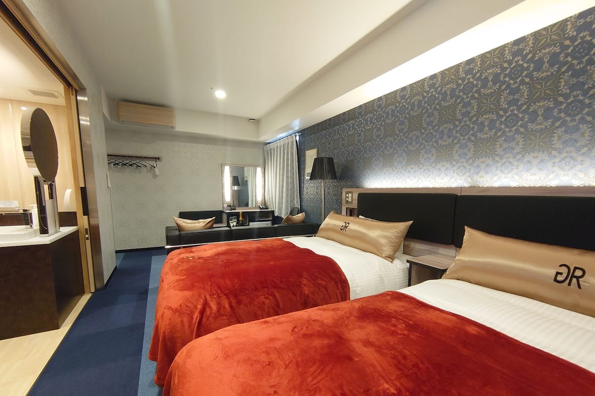 Ein Hotelzimmer mit zwei Betten, einem Schreibtisch, einem Spiegel und einem Badezimmer.