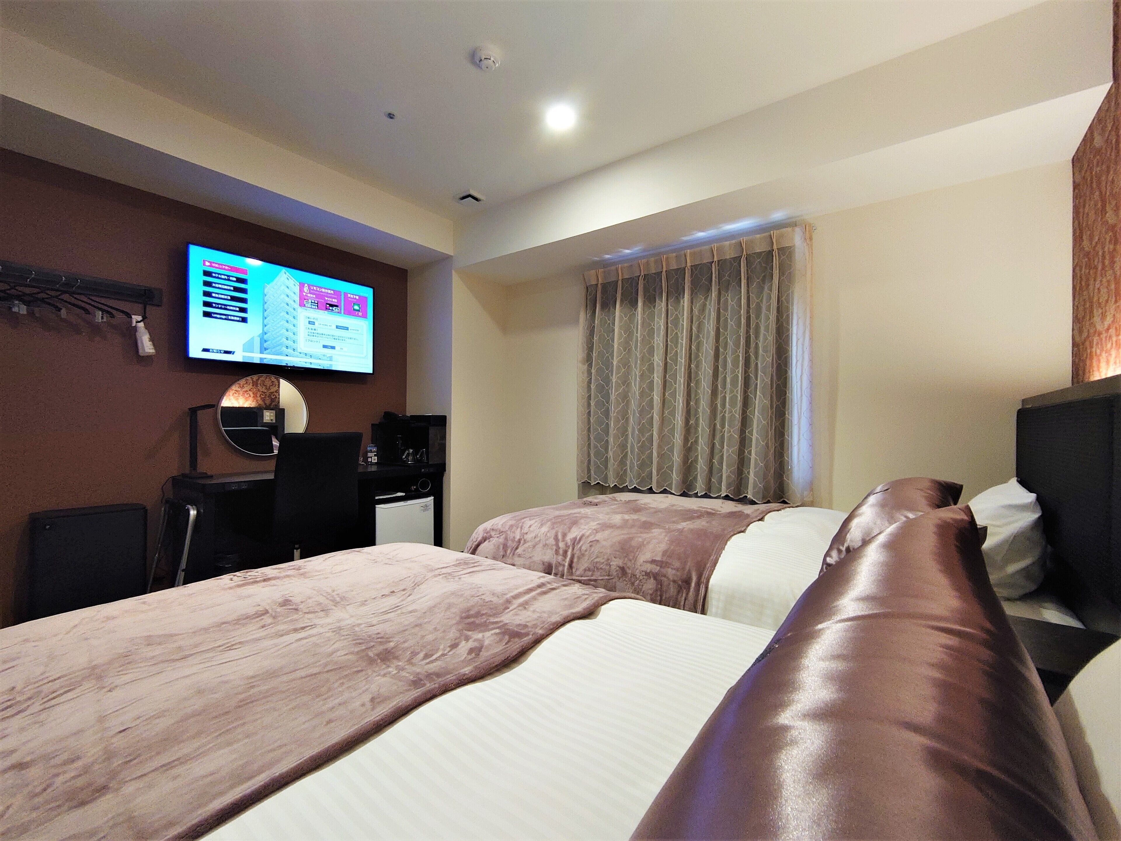A hotel room with two beds, a desk with a computer, a television, and a window with curtains.
