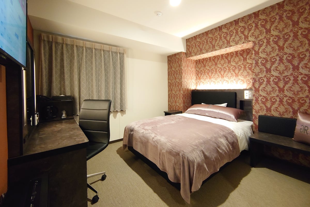 Ein Hotelzimmer mit Bett, Schreibtisch mit Stuhl, Fernseher und einer Wand mit Muster.