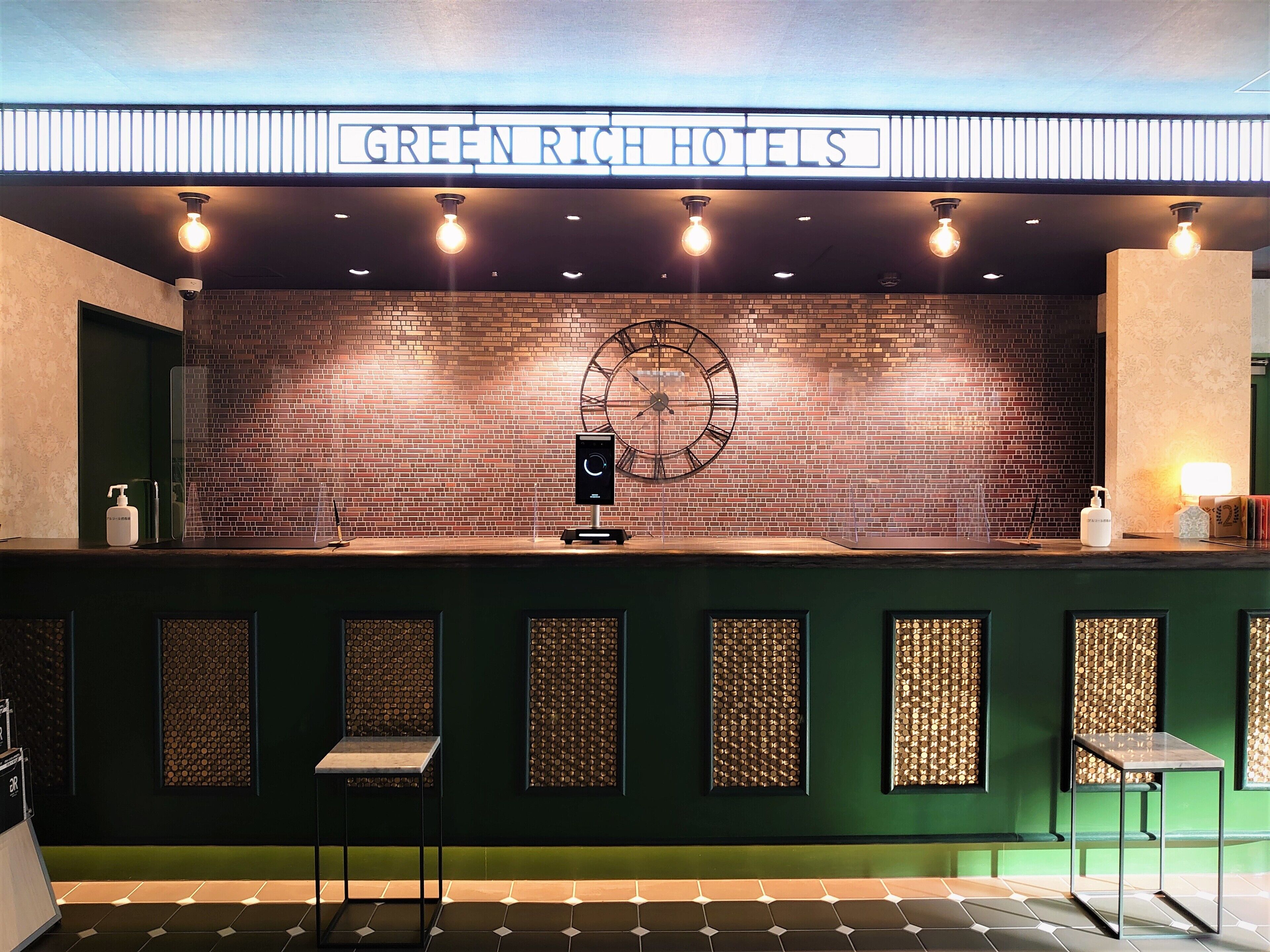 A reception desk at Green Rich Hotels with a brick wall backdrop, a clock, and a modern design.