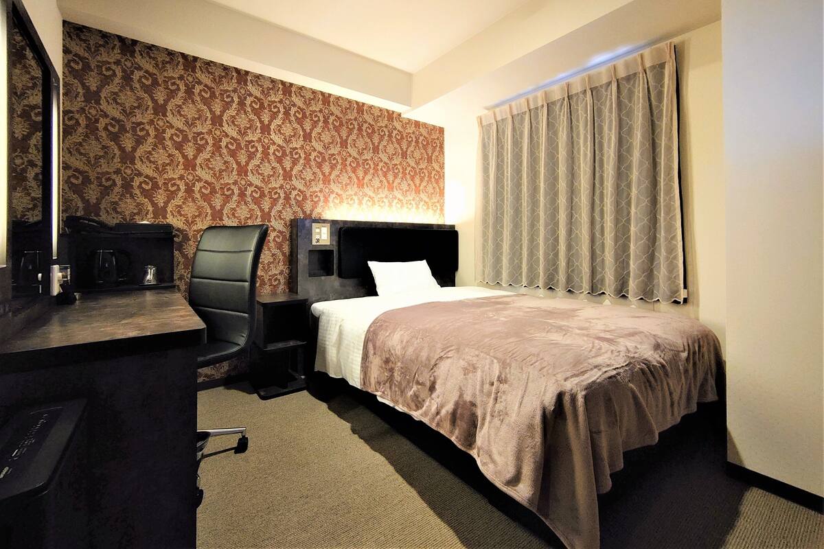 Ein Hotelzimmer mit einem Bett, einem Schreibtisch mit Stuhl, einem Nachttisch, einem Spiegel und einer Wand mit Muster.
