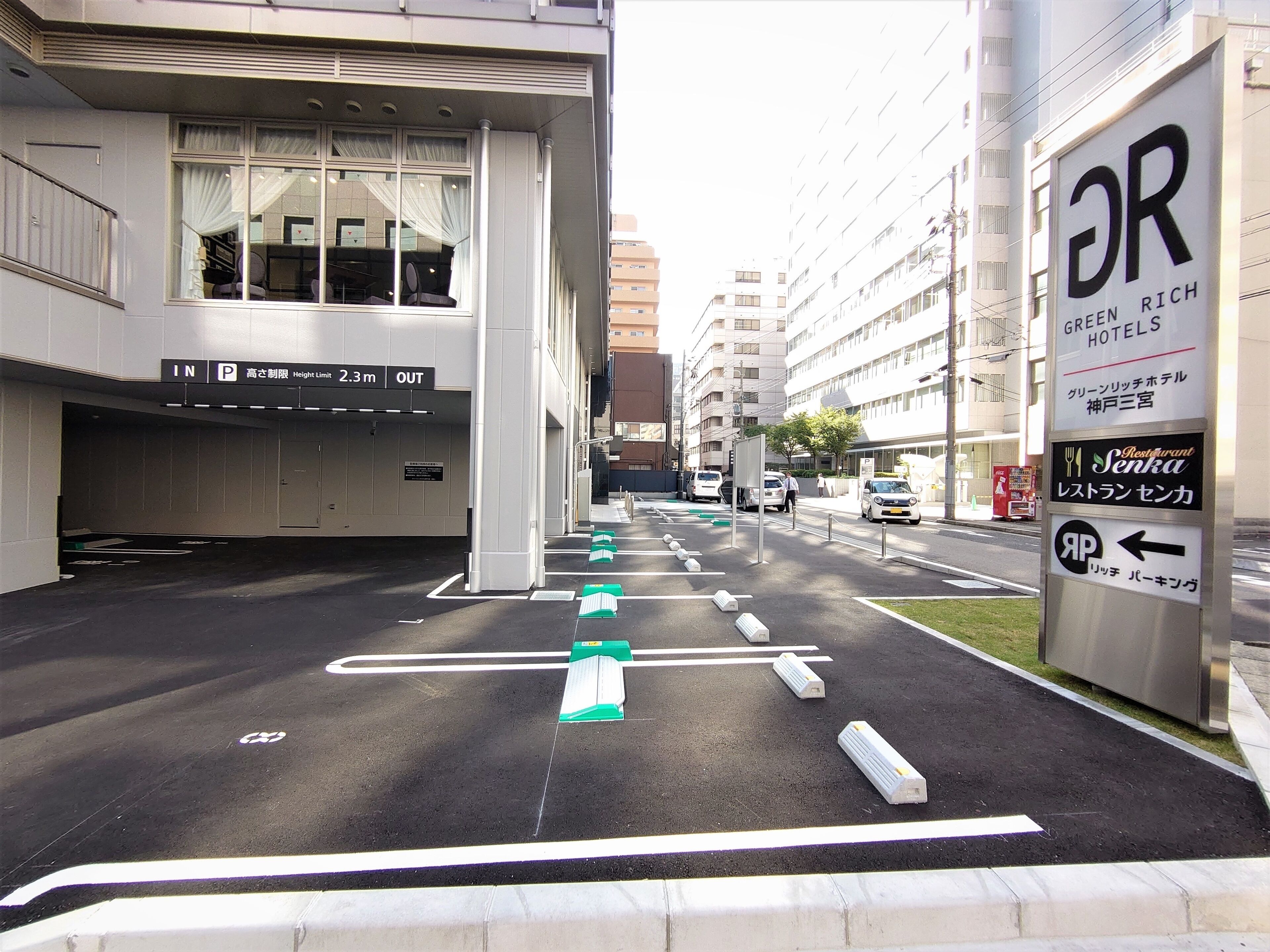 A parking lot with marked spaces, a building with a sign for 'Green Rich Hotels', and a pedestrian crossing.