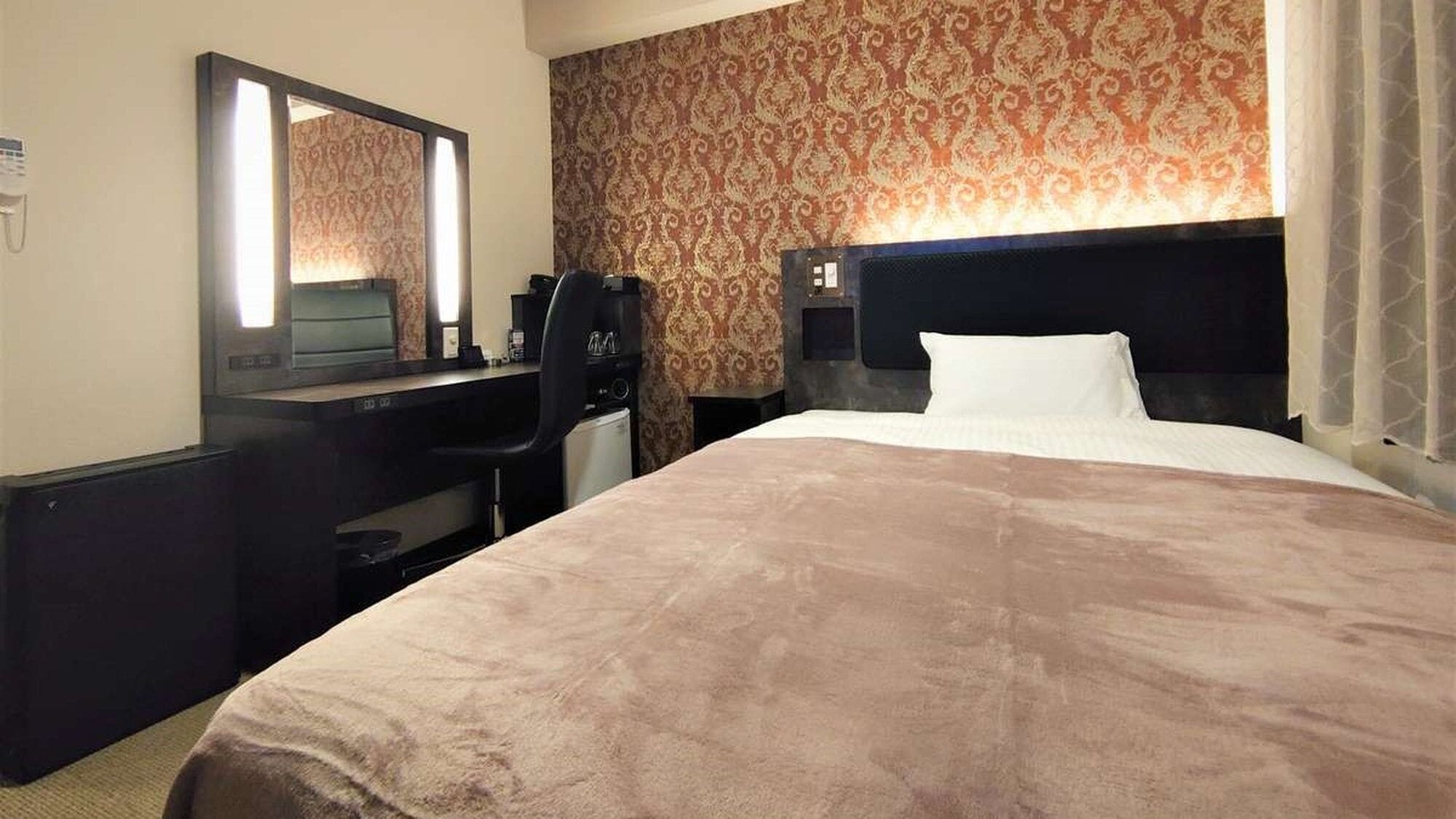Une chambre d’hôtel avec un grand lit, un bureau avec une chaise, un miroir et un mur décoré d’un motif.