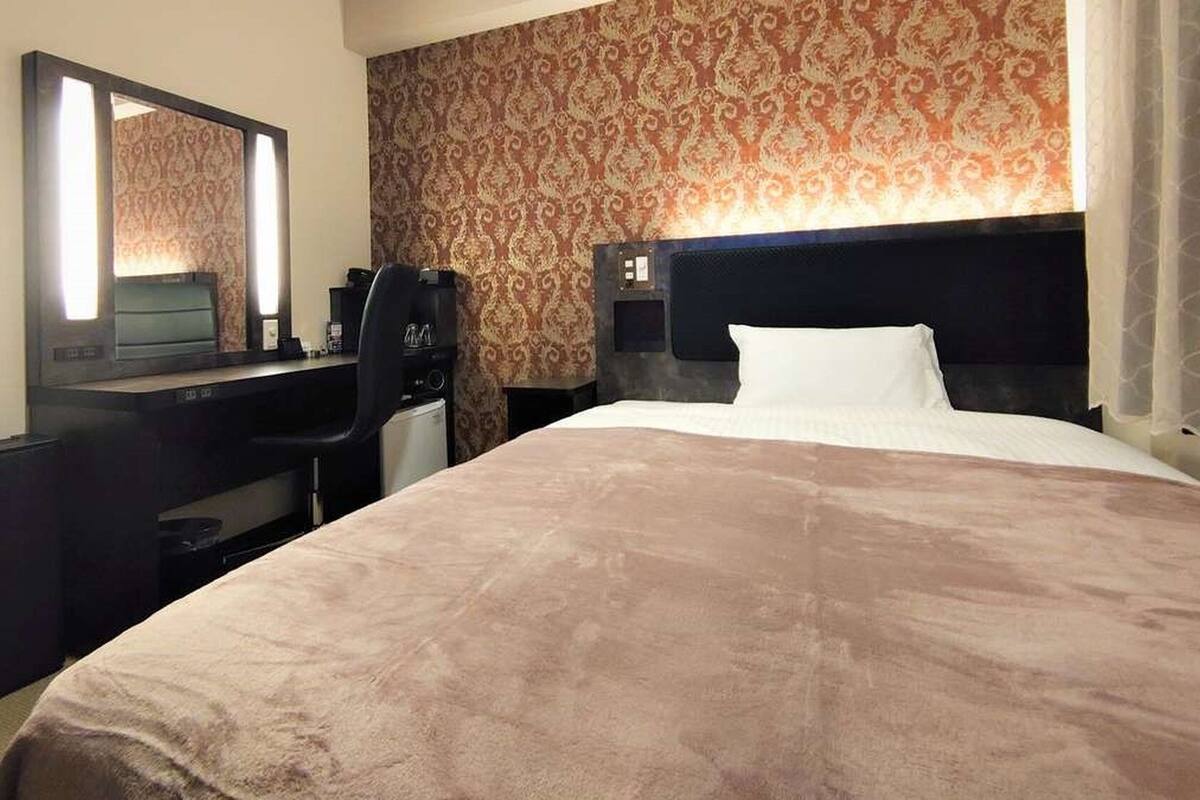 Ein Hotelzimmer mit einem großen Bett, einem Schreibtisch mit Stuhl, einem Spiegel und einer Wand mit Muster.