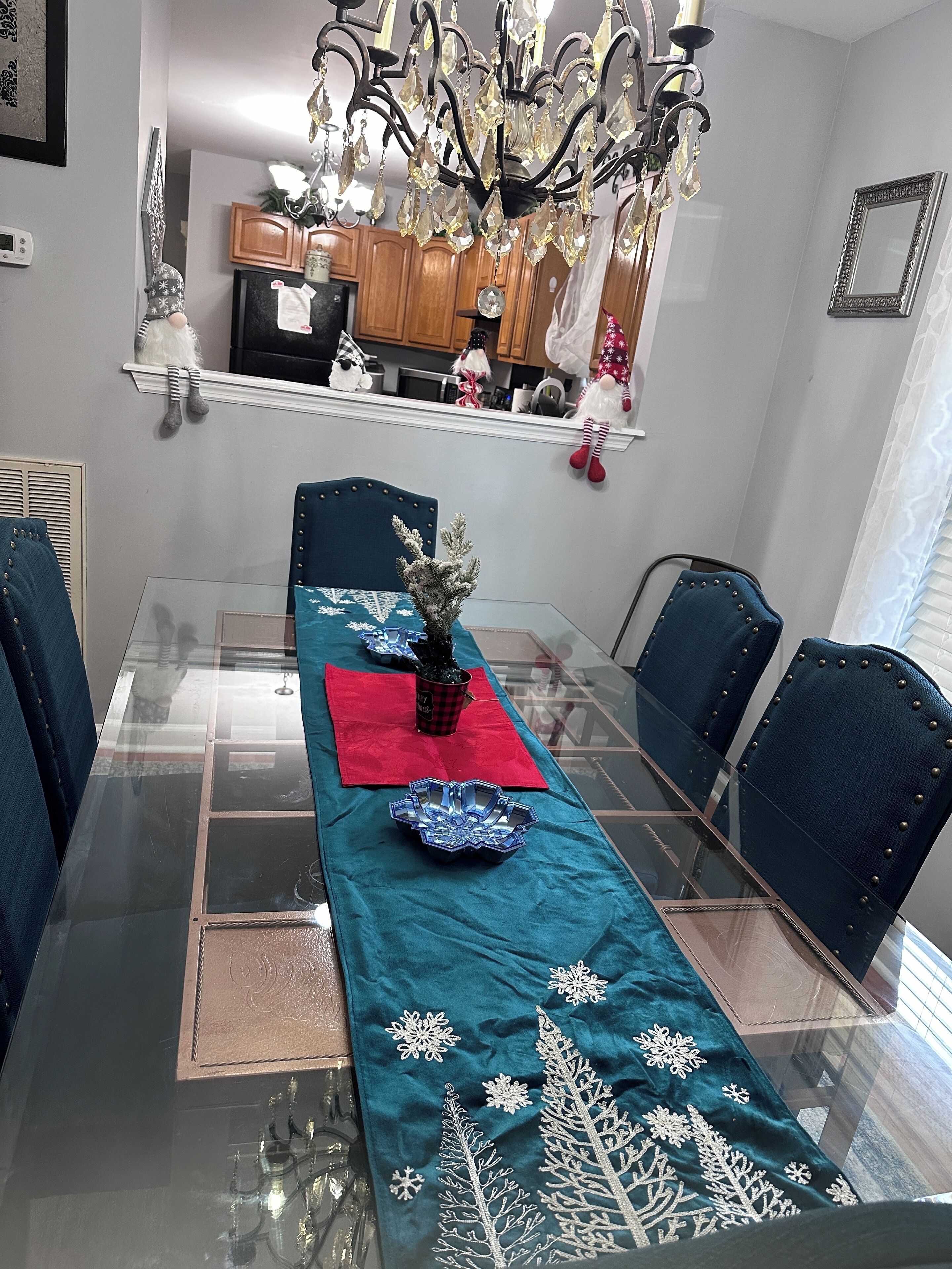 A dining area with a glass table, teal tablecloth with snowflake patterns, and a chandelier.