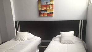 A room with two single beds, each with a white mattress and pillow, and a black headboard. - Aparthotel Navarra (San Miguel de Salcedo)
