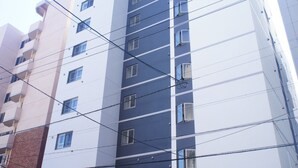 Un immeuble à plusieurs étages doté d’une architecture moderne, avec une façade composée d’un mélange de panneaux blancs et foncés, et un fourgon garé devant.