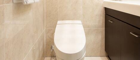 Un baño moderno con inodoro blanco, azulejos color beige, repisa de madera y un mueble oscuro.