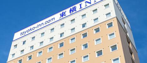 Een meerlaags hotelgebouw met een bord waarop 'toyoko-inn.com' en '東 様 INN' staat, wat de naam en locatie aangeeft.