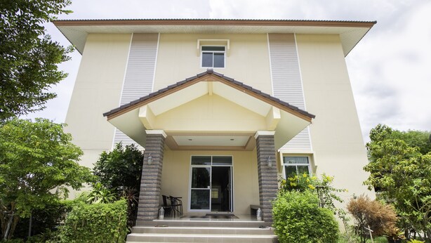 A two-story building with a beige facade, a central entrance with a small porch, and a set of stairs leading to the door.