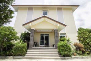 Ein zweistöckiges Gebäude mit einer beige gefärbten Fassade, einem zentralen Eingang mit einer kleinen Veranda und einer Treppe, die zur Tür führt.