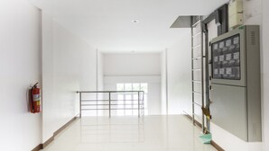 A corridor with a fire extinguisher, a metal railing, and a control panel on the right.