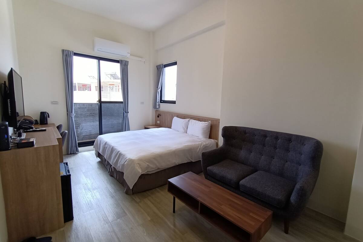 Ein Hotelzimmer mit Bett, einer Couch, einem Schreibtisch mit Computer und einem Fenster mit Vorhängen.