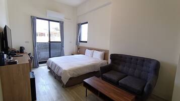 Una habitación de hotel con cama, sofá, escritorio con ordenador y ventana con cortinas.