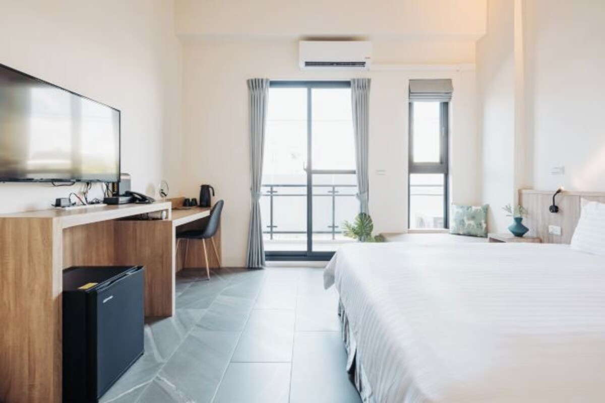 Ett hotellrum med en säng, ett skrivbord med en dator, en tv och ett litet kylskåp.