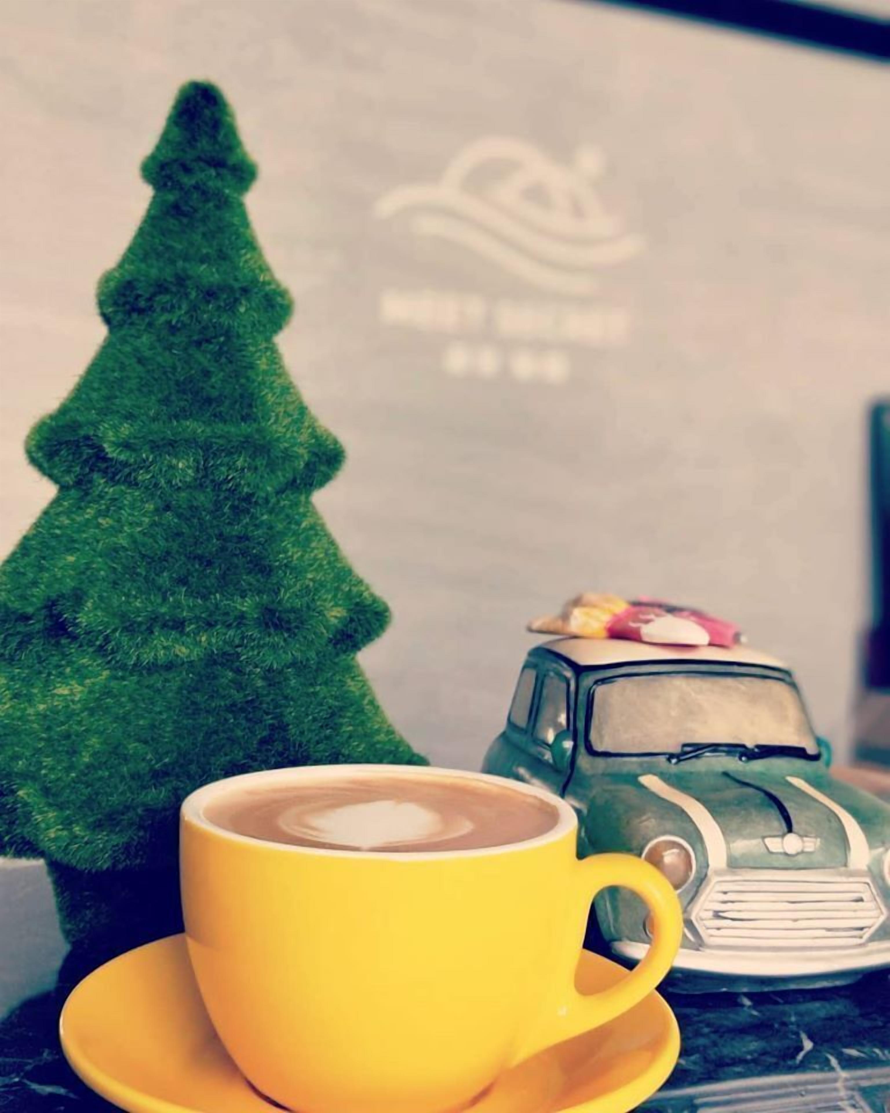 Een gele koffiekop op een schotel, een kleine groene kerstboom en een peper-en-zoutstrooier in de vorm van een oldtimer.