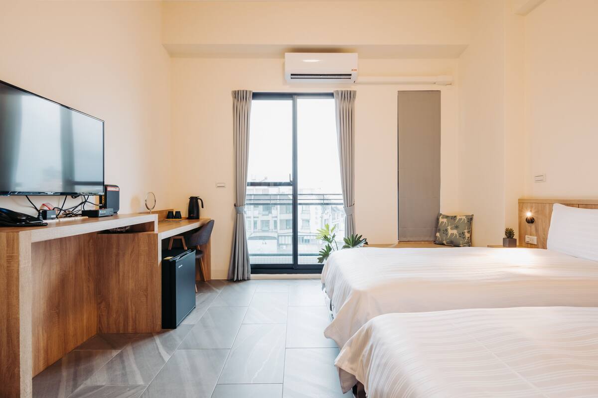 Ein Hotelzimmer mit einem Bett, einem Schreibtisch mit Fernseher und einem Fenster mit Vorhängen.
