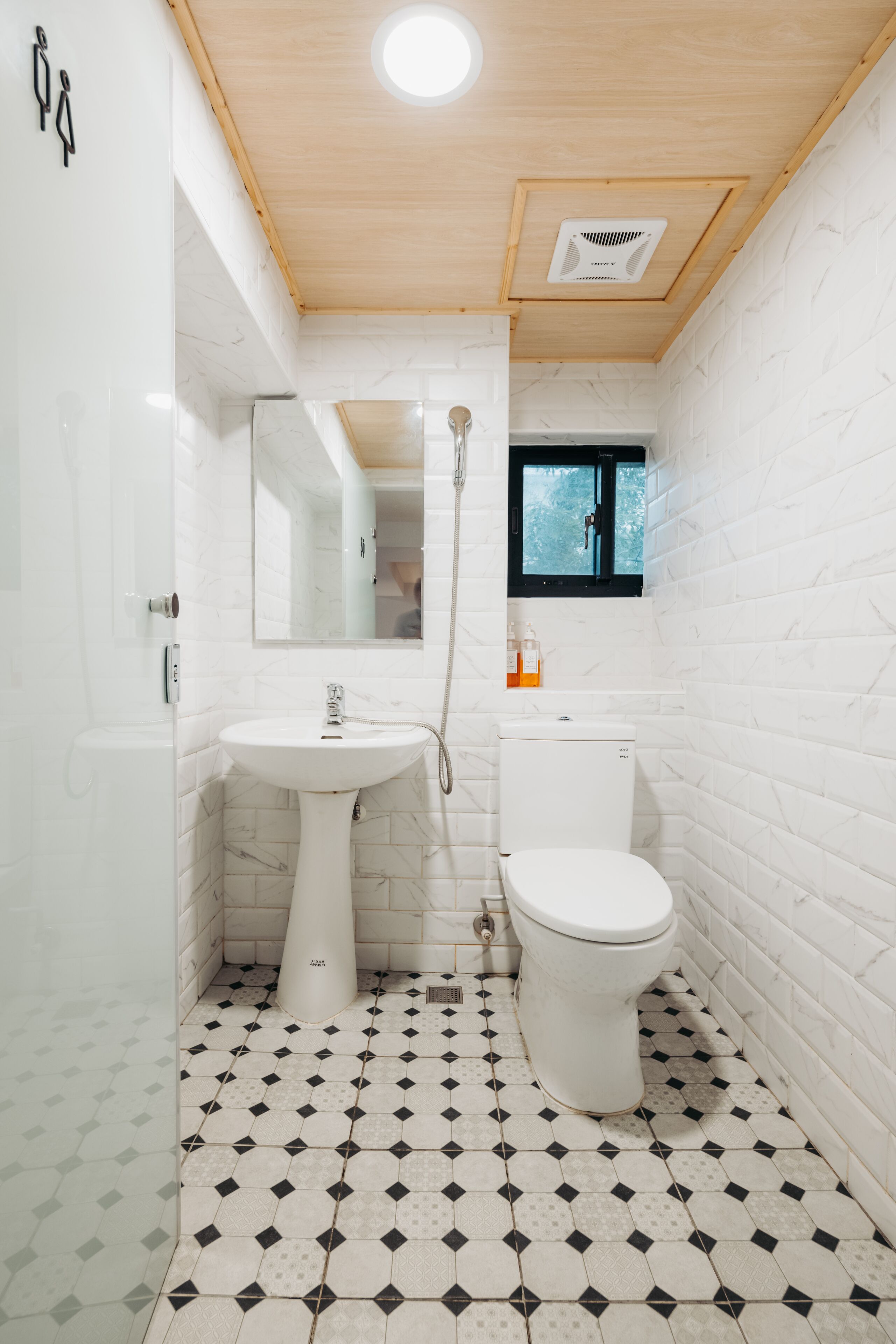 A compact bathroom with a white sink, toilet, and shower. The floor has a geometric tile pattern.