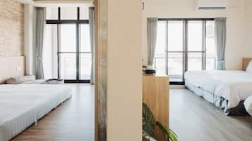 A modern hotel room with two beds, large windows with curtains, a wooden floor, and an air conditioning unit.
