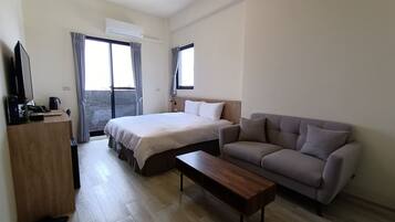 A hotel room with a bed, a sofa, a wooden coffee table, a desk with a computer and phone, and a TV.